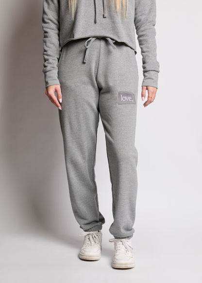 Person wearing gray sweatpants with 'love' patch on a plain background