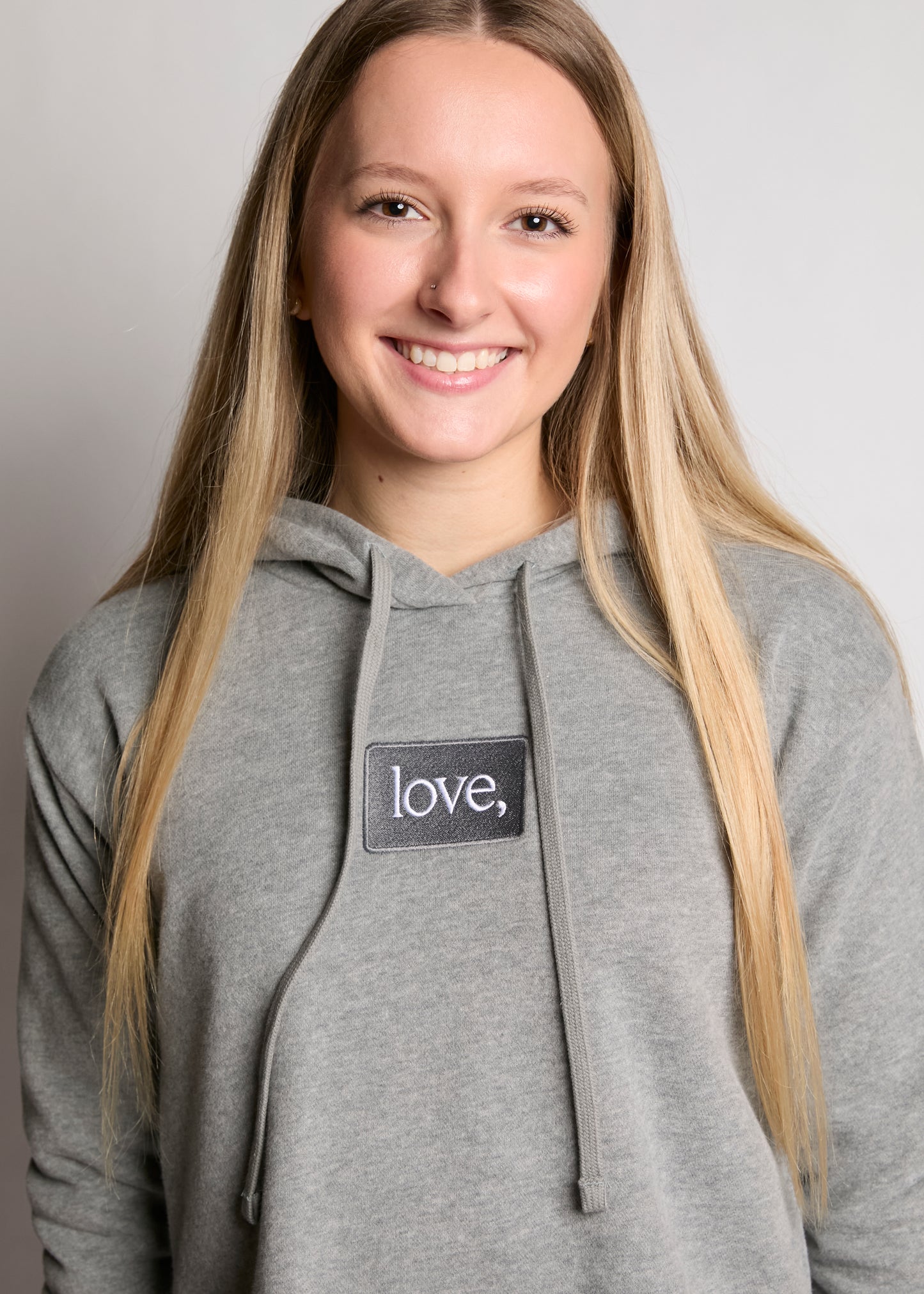 Person wearing a gray hoodie with a 'love' patch on a plain background