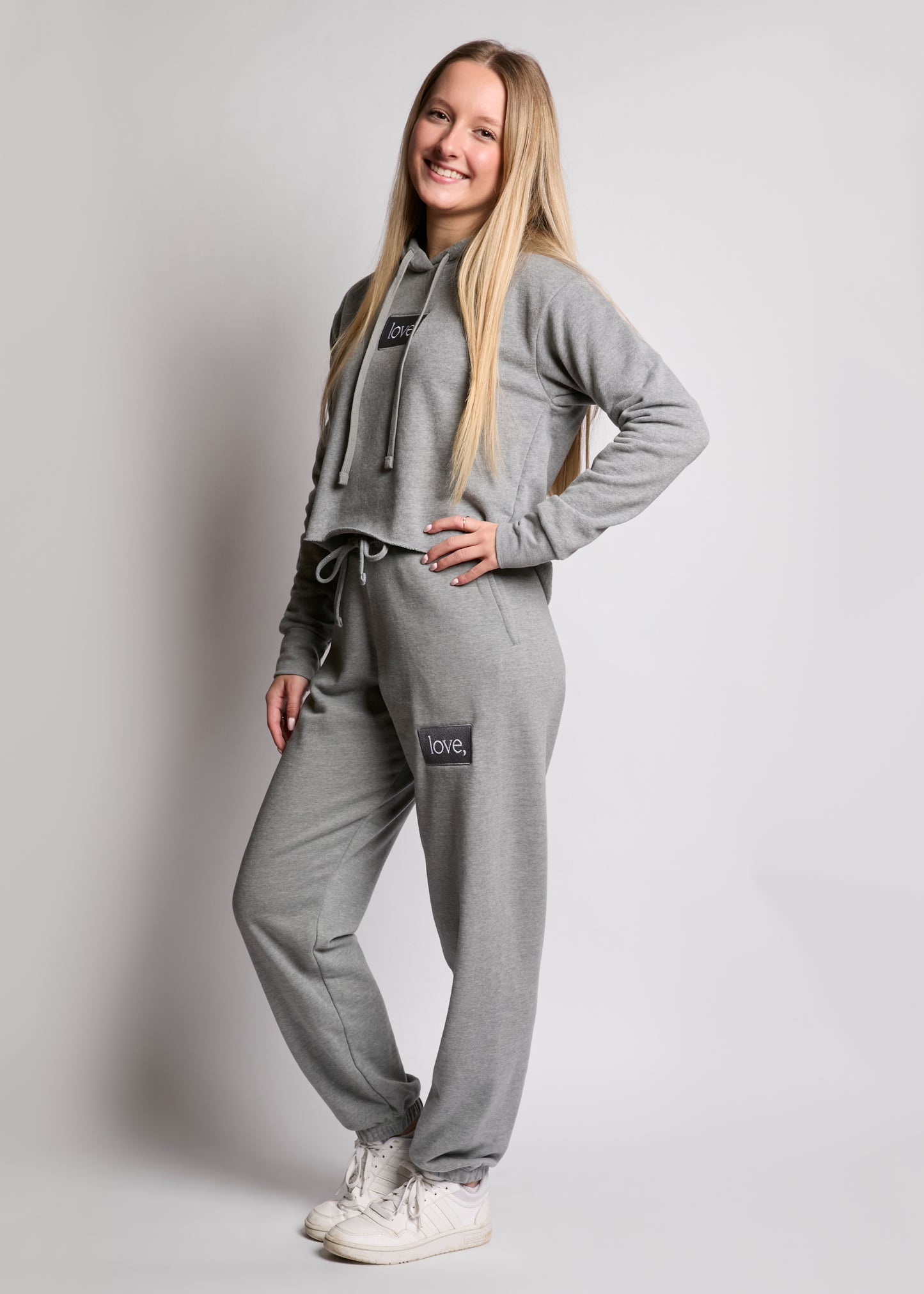 Person wearing a gray tracksuit with brand logos on a plain background