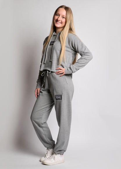 Person wearing a gray tracksuit with brand logos on a plain background