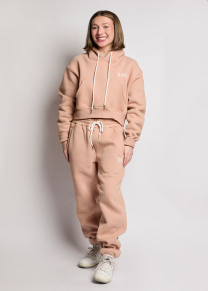 Person wearing a beige tracksuit with 'LOVE' on the hoodie against a plain background