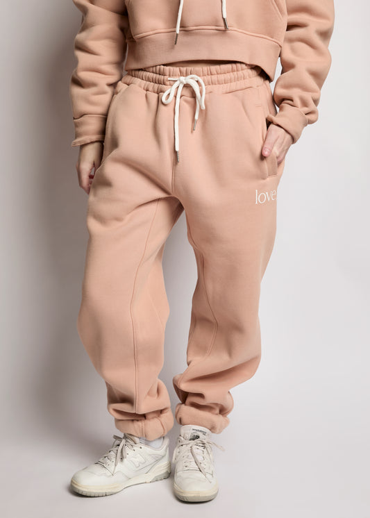 Person wearing a beige tracksuit with 'love' text on pants against a plain background
