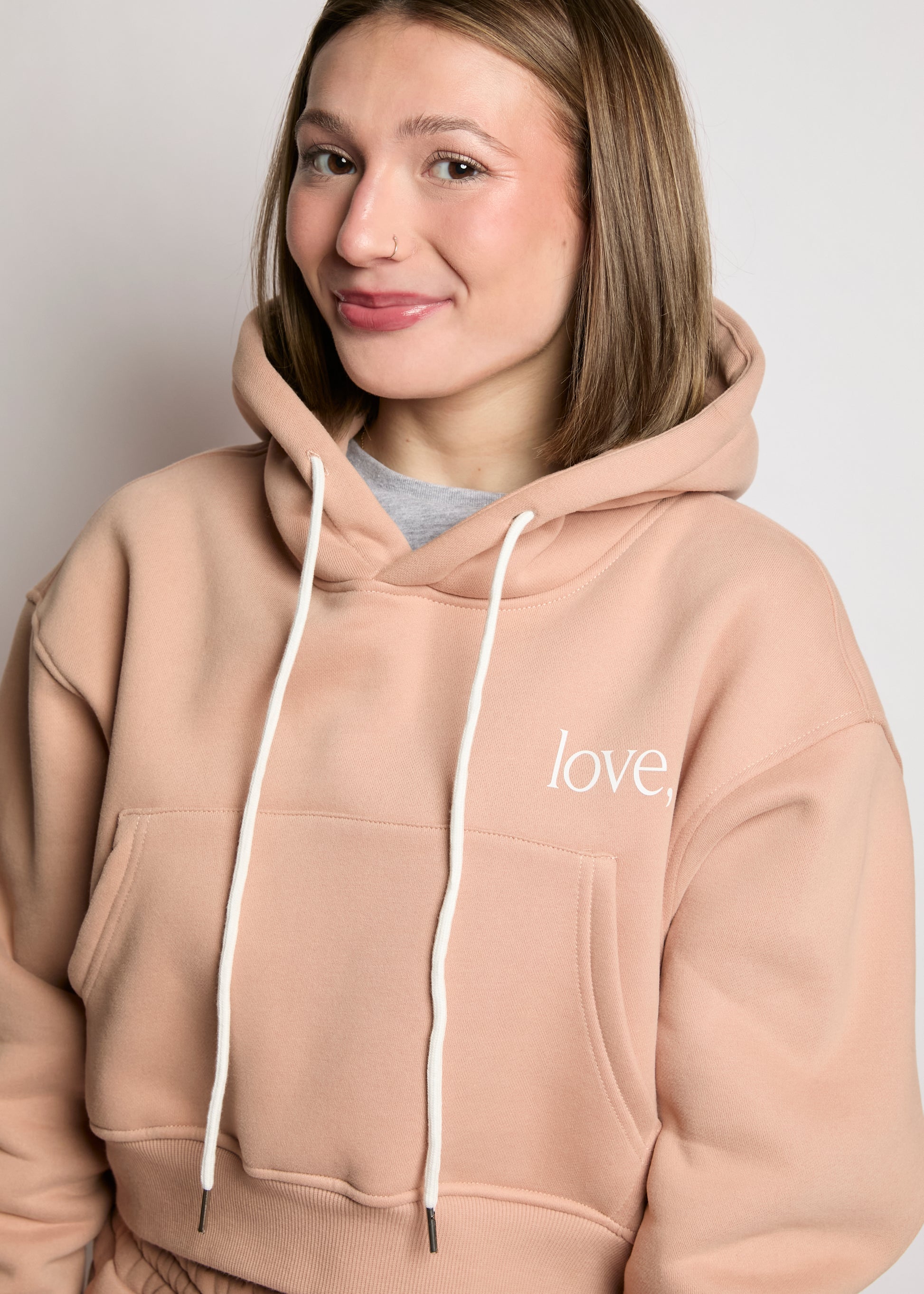 Person wearing a beige hoodie with 'love' printed on it against a plain background
