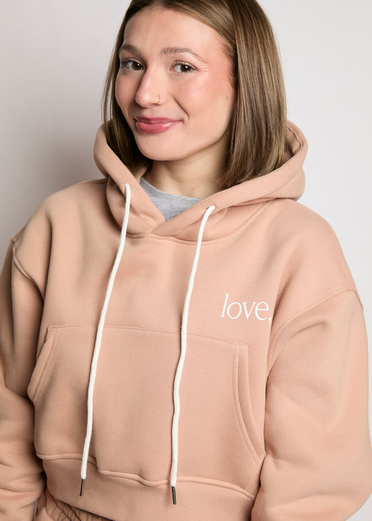 Person wearing a beige hoodie with 'love' printed on it against a plain background