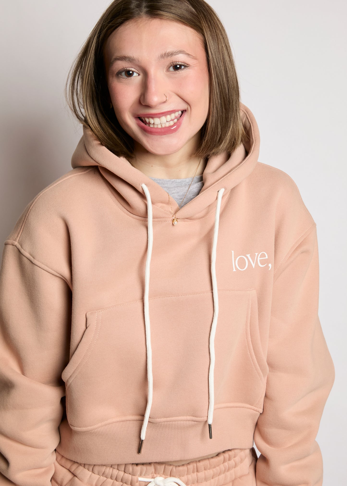 Person wearing a beige hoodie with 'love.' text on a plain background