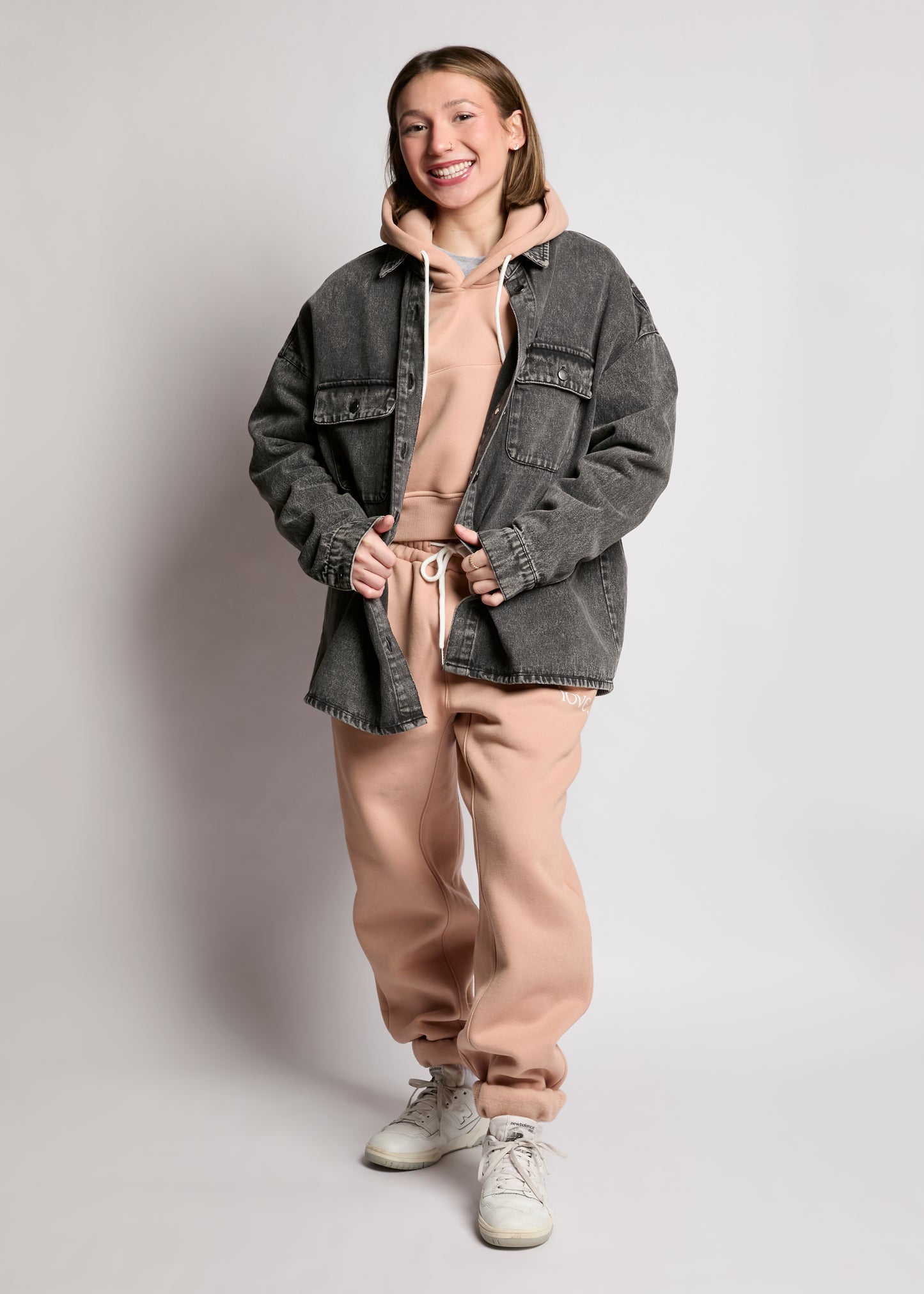 Person wearing a gray jacket over a beige hoodie and pants on a plain background