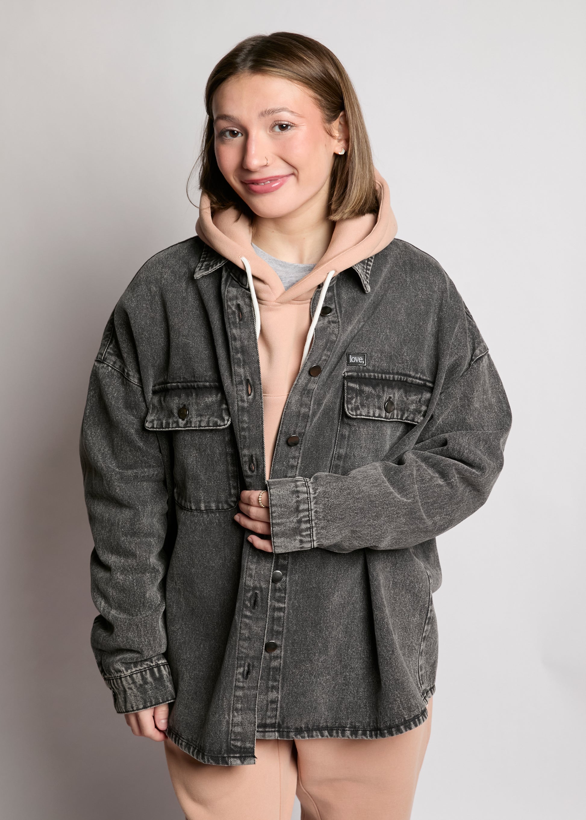 Person wearing a gray denim jacket over a hoodie on a plain background