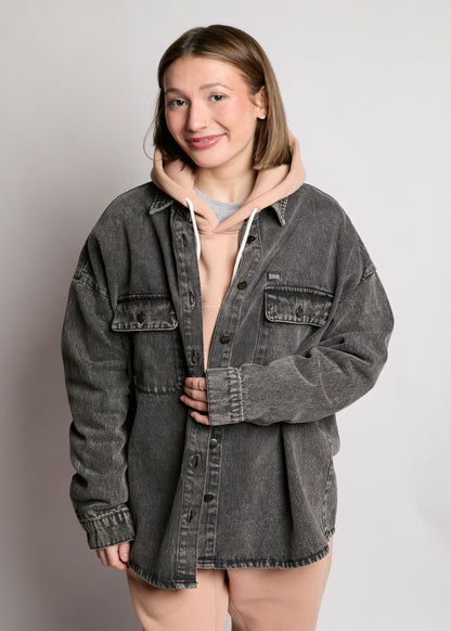 Person wearing a gray denim jacket over a hoodie on a plain background