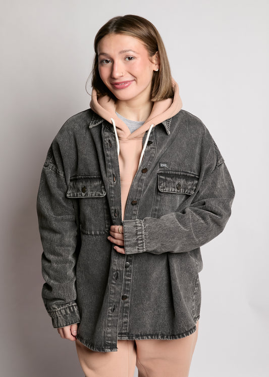 Person wearing a gray denim jacket over a hoodie on a plain background