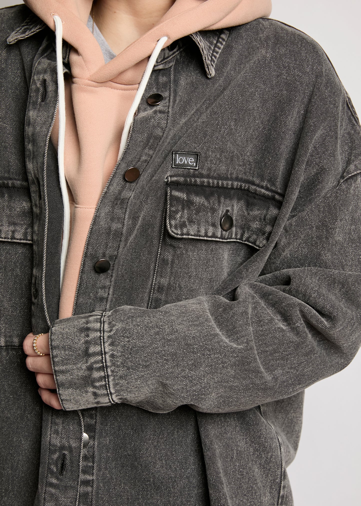 Person wearing a gray denim jacket with a brand label on a plain background