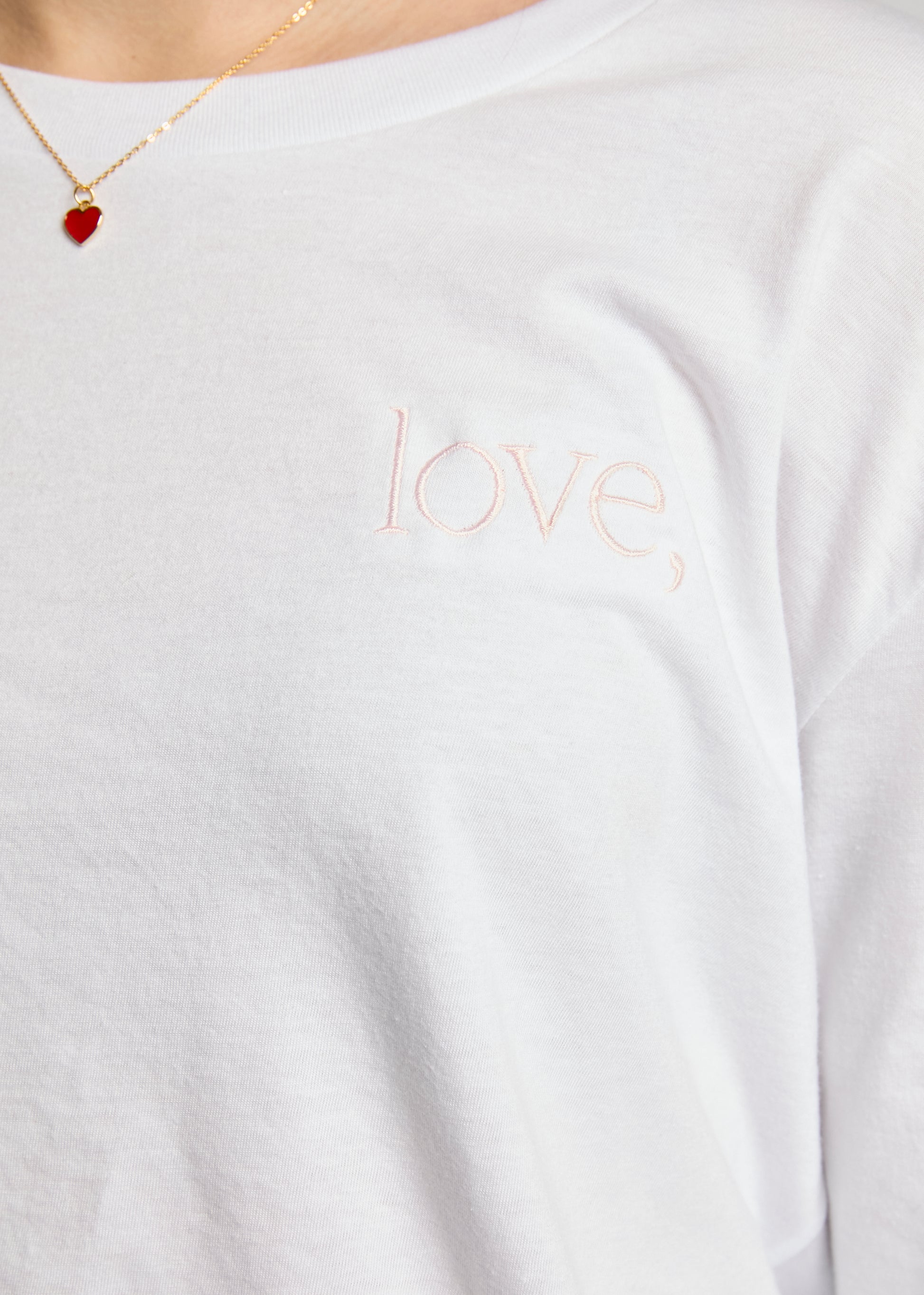 White shirt with 'love' embroidery, worn by a person, with a necklace featuring a red heart pendant.