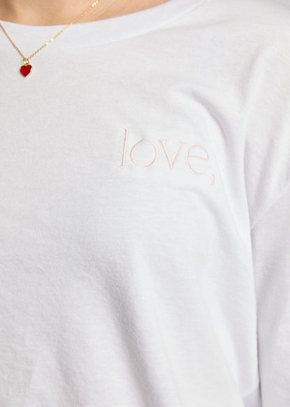 White shirt with 'love' embroidery, worn by a person, with a necklace featuring a red heart pendant.