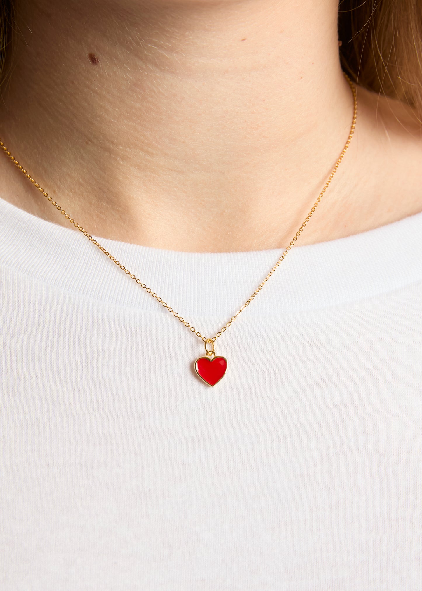 Gold necklace with a red heart pendant on a white background