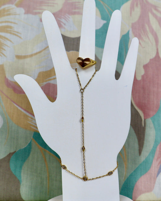 A delicate gold Y-necklace with a small heart-shaped charm on the top loop, displayed on a white hand-shaped jewelry stand against a floral fabric background.