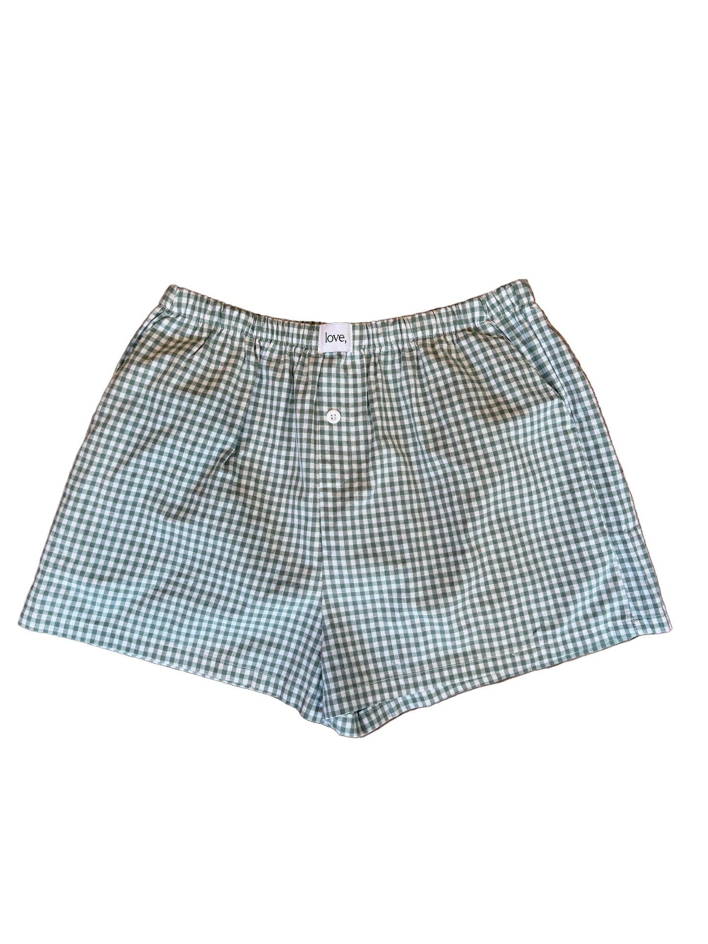 A pair of gingham shorts in a green and white checkered pattern, The shorts feature an elastic waistband with a single white button and side pockets.