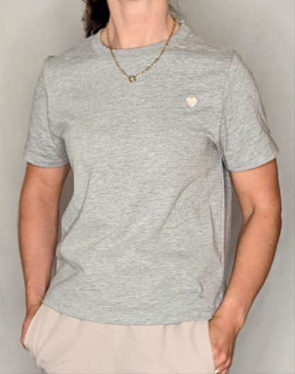 Person wearing a gray t-shirt with a small logo on a plain background