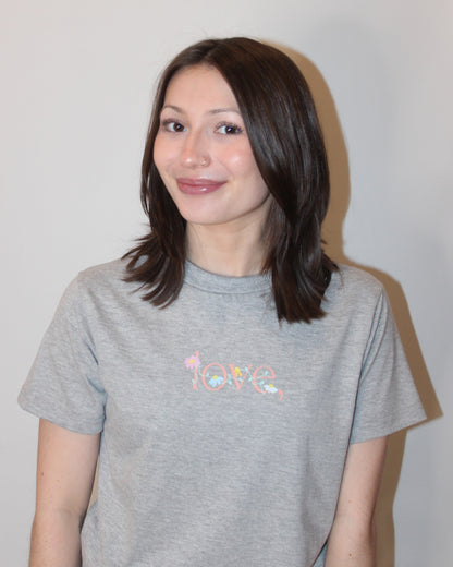 love, logo wrapped in floral multi colored vine printed across the chest on a light grey crew tee. 