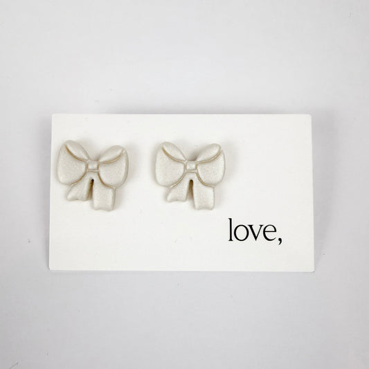 Bow-shaped earrings on a card with 'love' text against a light gray background