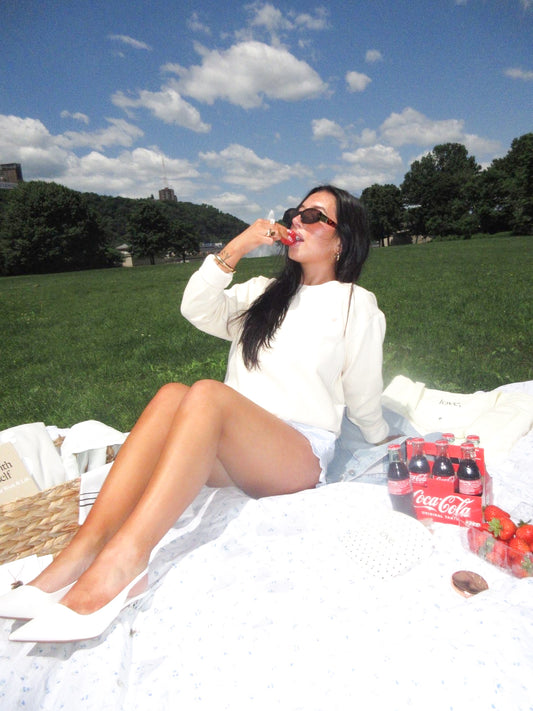 Woman sitting on a blanket in a park with Coca-Cola bottles and strawberries.