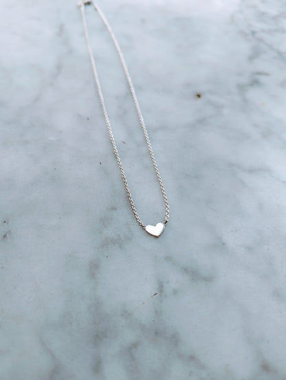 A small heart-shaped sterling silver necklace on a delicate chain, displayed on a marble surface.