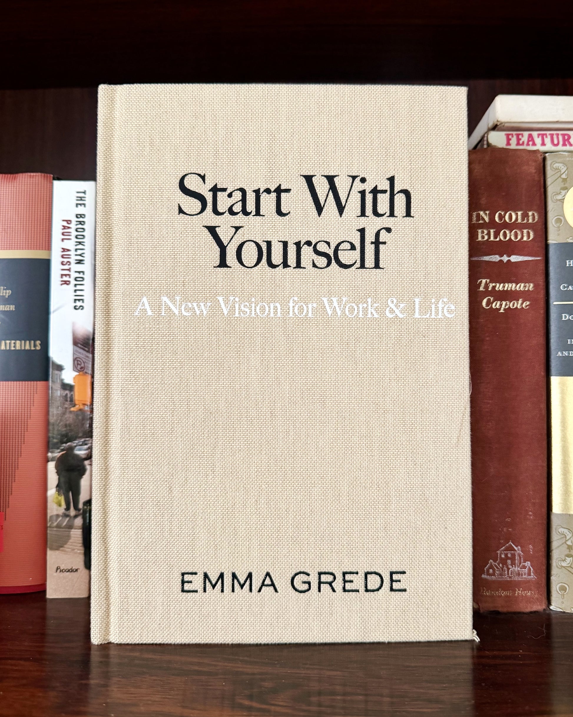 Book titled 'Start With Yourself' by Emma Grede among other books on a wooden surface.