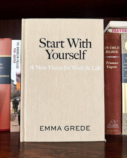 Book titled 'Start With Yourself' by Emma Grede among other books on a wooden surface.