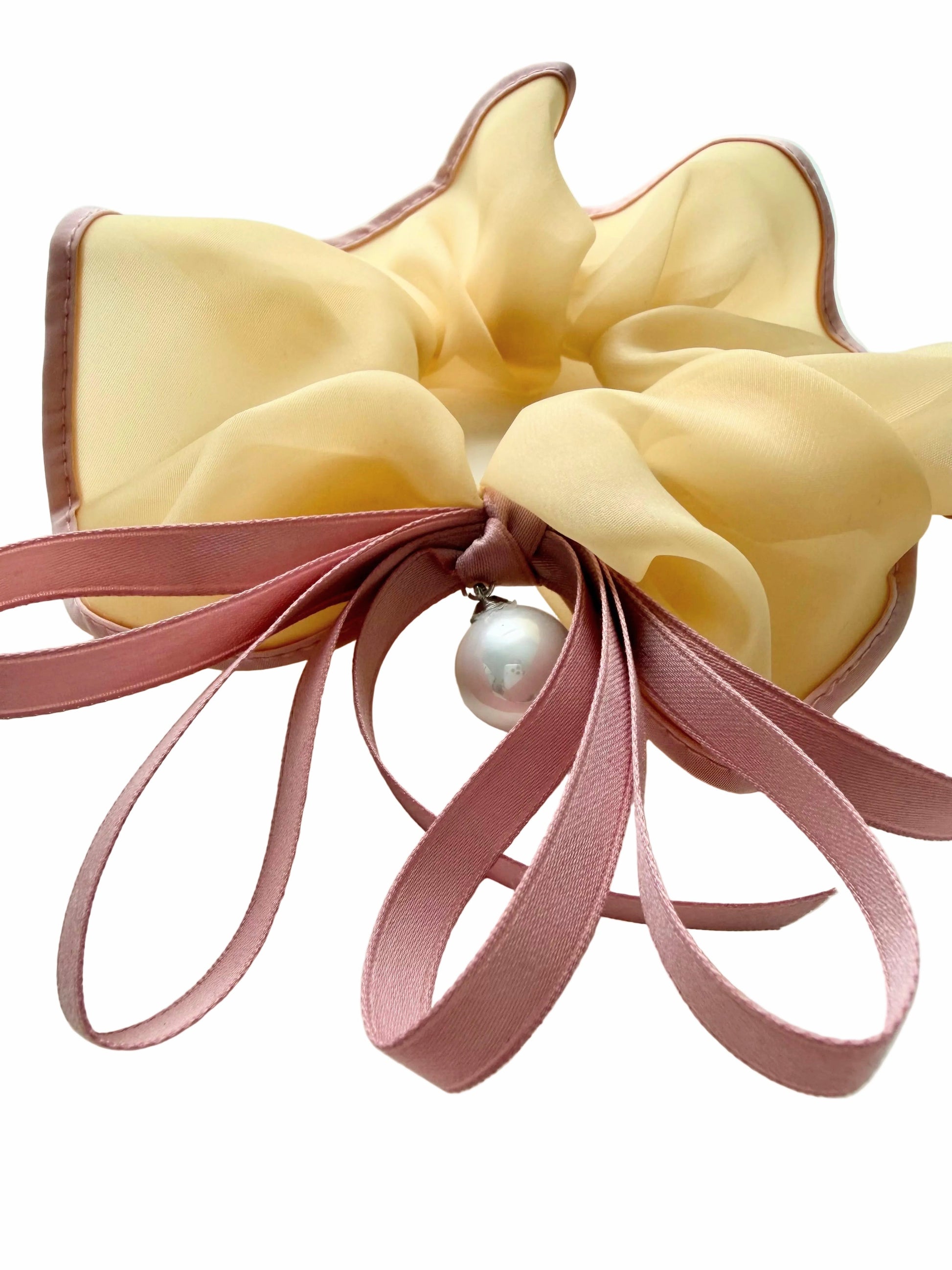 Yellow bow hair clip with pink ribbons and a pearl on a white background