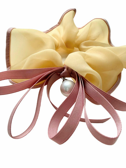 Yellow bow hair clip with pink ribbons and a pearl on a white background