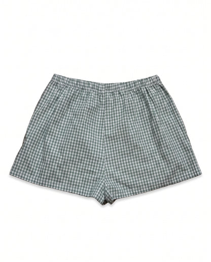A pair of men's shorts featuring a green and white gingham checkered pattern, laid flat against a solid white background.