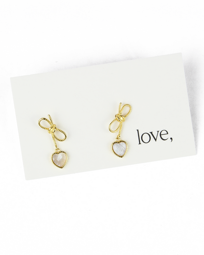 Gold earrings with heart-shaped charms on a white card with 'love' text.