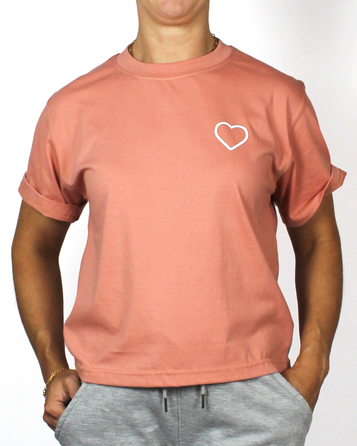 Person wearing a pink t-shirt with a white heart design on a plain background