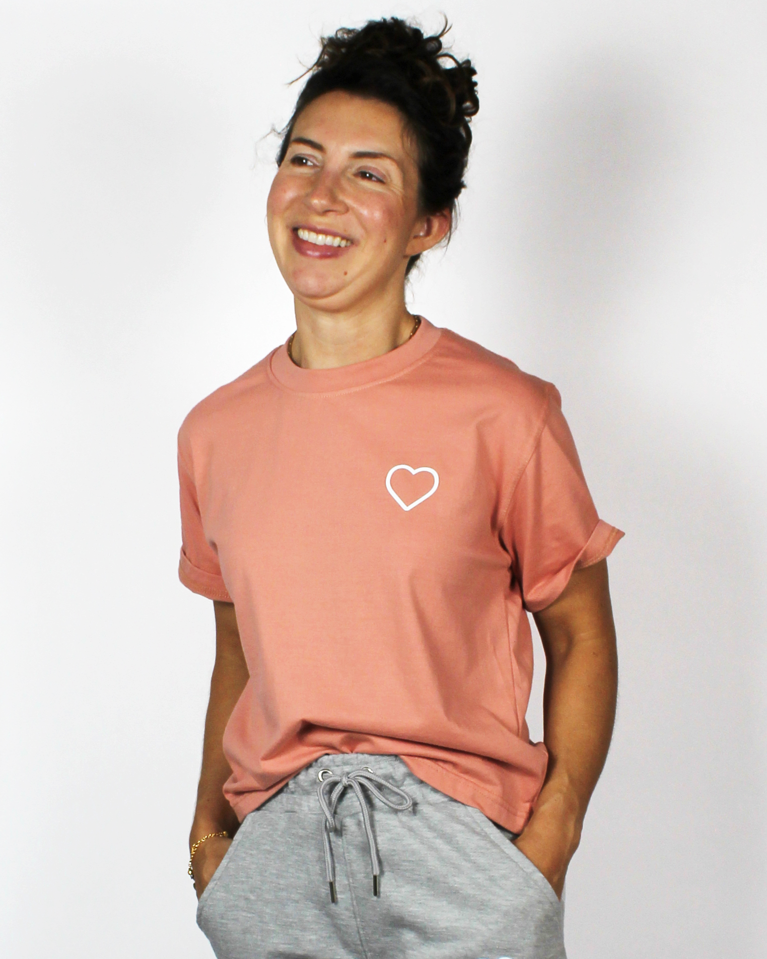 Person wearing a pink t-shirt with a heart design on a plain background