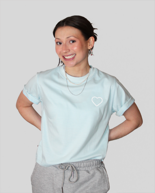 Person wearing a light blue t-shirt with a heart logo on a plain background