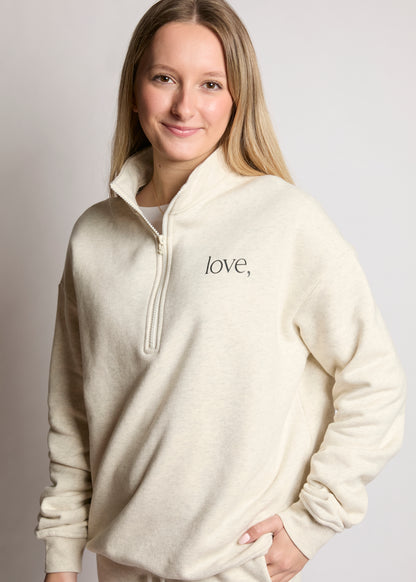 Woman wearing a cream-colored pullover with 'love' embroidered on it against a plain background