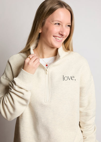 Woman wearing a cream-colored pullover with 'love' embroidered on it against a plain background