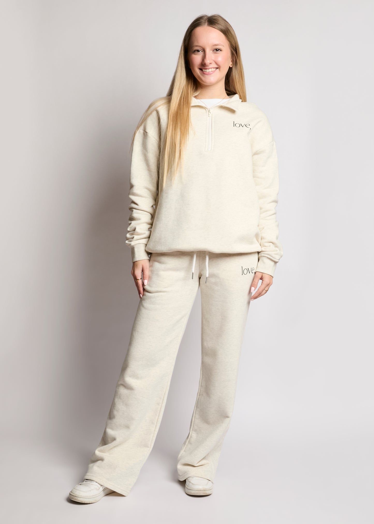 Person wearing a beige hoodie and pants set on a plain background
