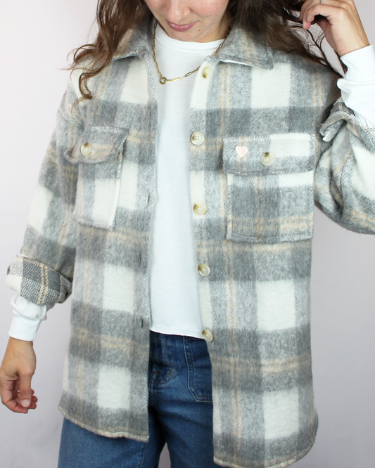 Person wearing a plaid shirt over a white sweater with a plain background