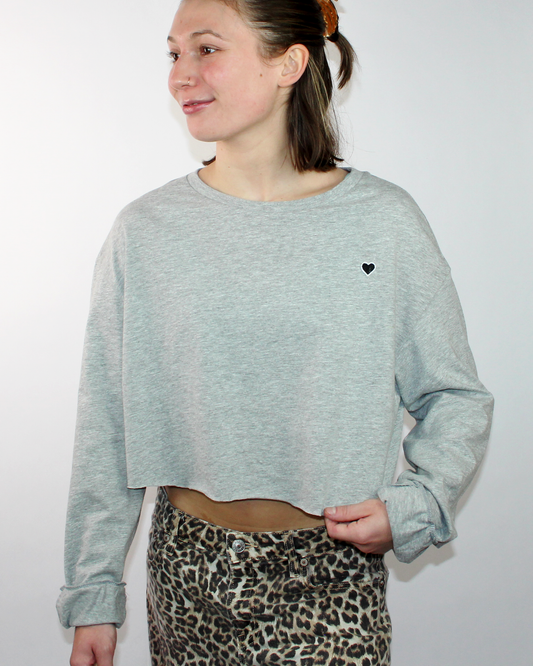 Person wearing a light gray cropped sweatshirt with a black heart on a white background