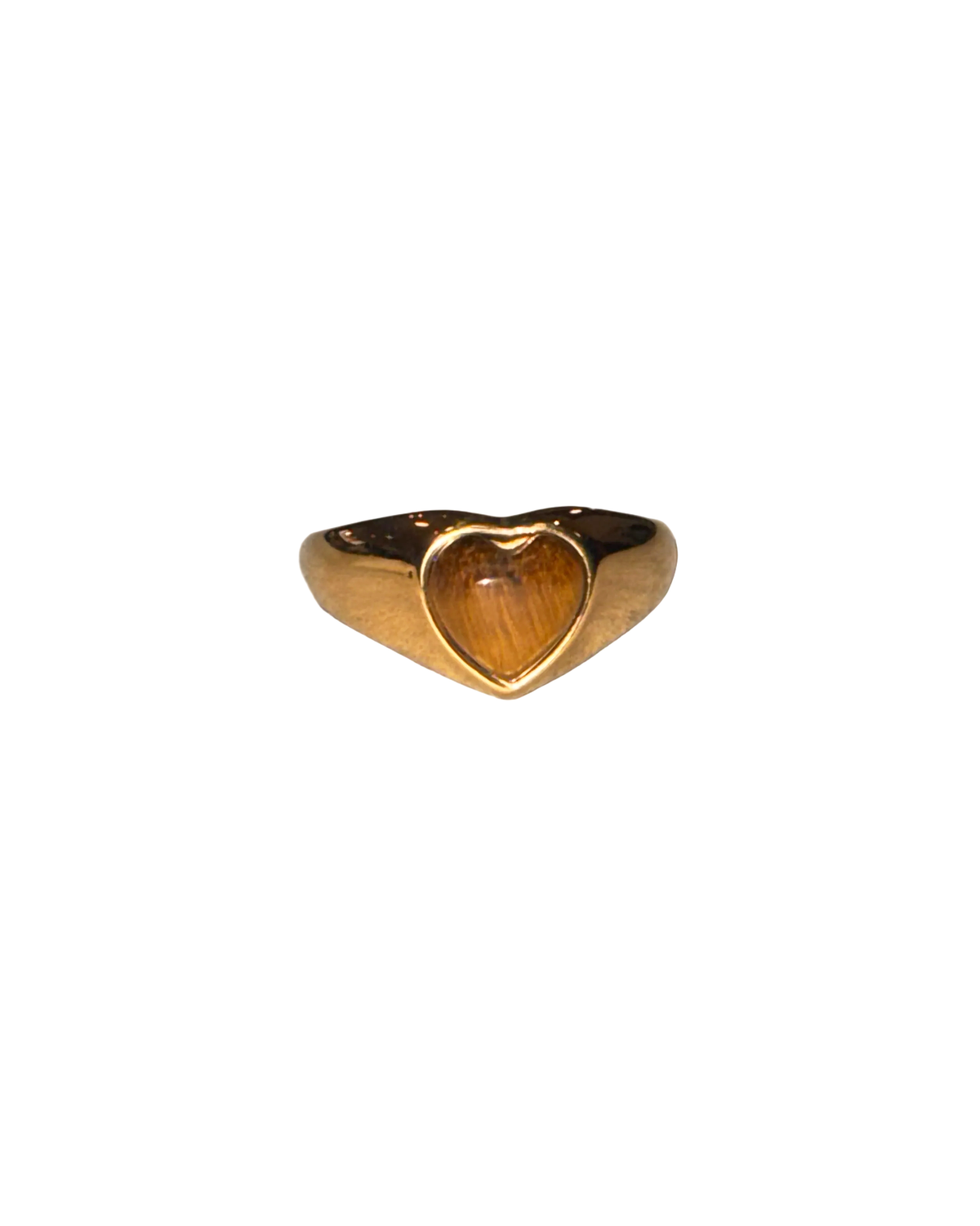 A gold signet ring with a heart-shaped face, featuring a warm brown tiger's eye inlay, resting on a textured light gray surface.